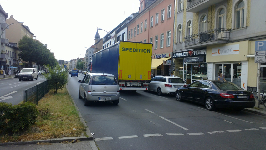 Blick auf Fahrspur mit einer Spur parkender Auto, einer Spur mit einem großen LKW und einer Spur mit PKW.